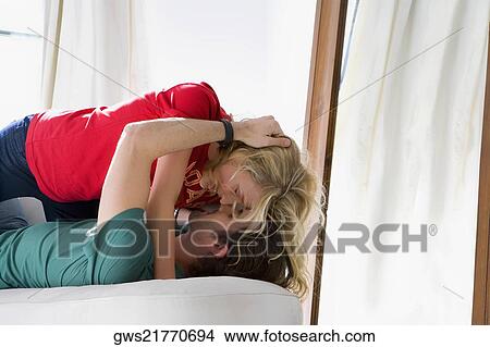Picture - Side profile of a young couple romancing on a couch. Fotosearch