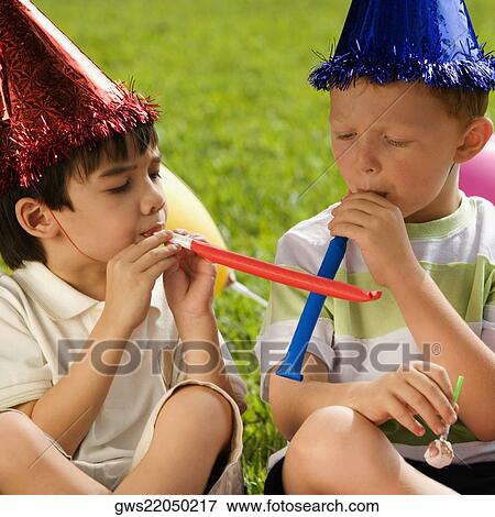 Stock Photo - Two boys sitting together and blowing party horns. Fotosearch