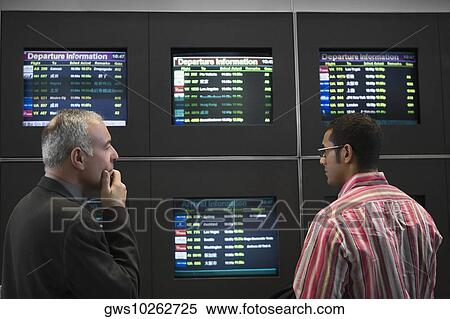 Stock Photography - Two businessmen looking at an arrival departure board at an airport. Fotosearch