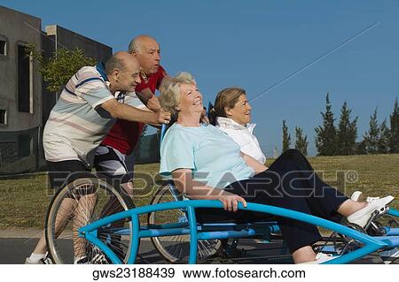 Two senior women sitting on a quadracycle and two senior men pushing it View Large Photo Image Stock Photo - Two senior women sitting on a quadracycle and two senior men pushing it. Fotosearch