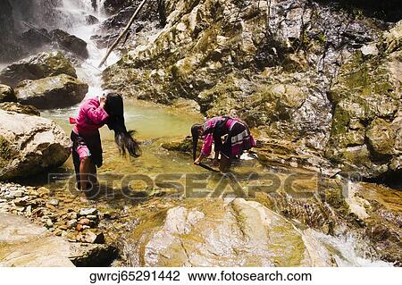 Stock Image - Two women washing hair at a waterfall, Jinkeng Terraced Field, Guangxi Province, China. Fotosearch