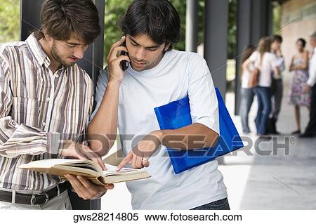 Two young men looking at a book in a corridor View Large Photo Image Stock Photography - Two young men looking at a book in a corridor. Fotosearch