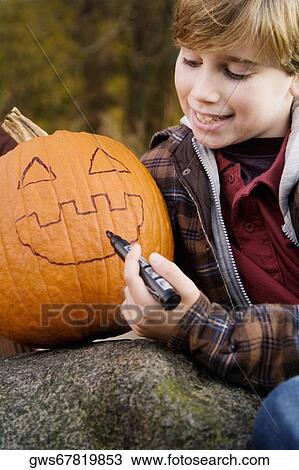 Boy drawing a human face on a pumpkin View Large Photo Image Stock Image - Boy drawing a human face on a pumpkin. Fotosearch