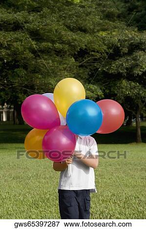 Boy holding balloons in a park View Large Photo Image Stock Photo - Boy holding balloons in a park. Fotosearch