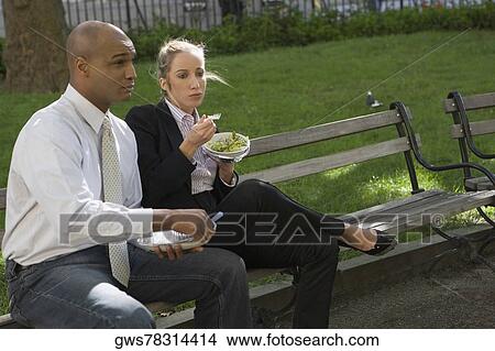Businessman and a businesswoman having food on a park bench View Large Photo Image Picture - Businessman and a businesswoman having food on a park bench. Fotosearch