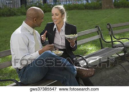 Businessman and a businesswoman having food on a park bench View Large Photo Image Stock Photo - Businessman and a businesswoman having food on a park bench. Fotosearch