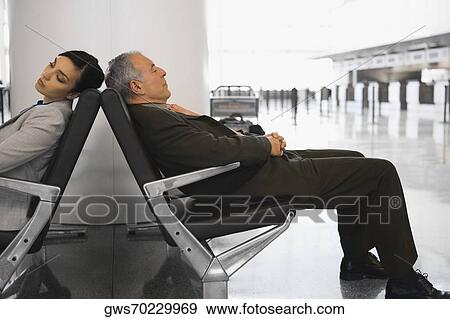 Stock Photo - Businessman and a businesswoman sleeping on chairs at an airport. Fotosearch