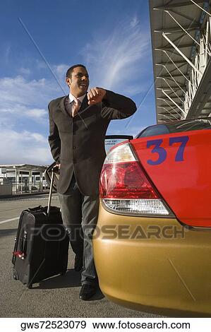 Stock Photo - Businessman checking the time near a taxi outside an airport. Fotosearch