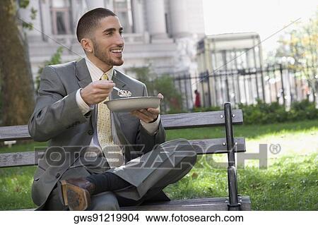 Businessman having food on a park bench View Large Photo Image Picture - Businessman having food on a park bench. Fotosearch