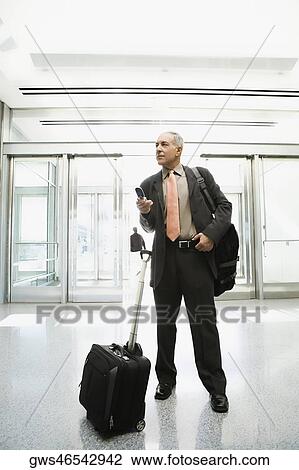 Businessman holding a mobile phone at an airport View Large Photo Image Stock Image - Businessman holding a mobile phone at an airport. Fotosearch