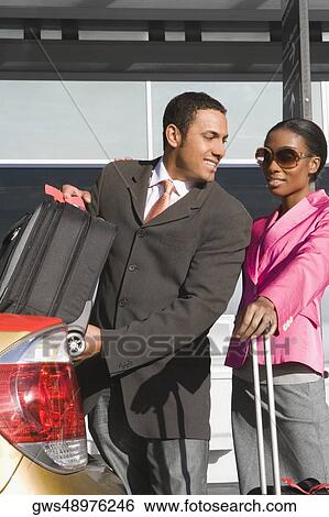 Businessman loading his suitcase on a car trunk with a businesswoman standing beside him View Large Photo Image Stock Photograph - Businessman loading his suitcase on a car trunk with a businesswoman standing beside him. Fotosearch