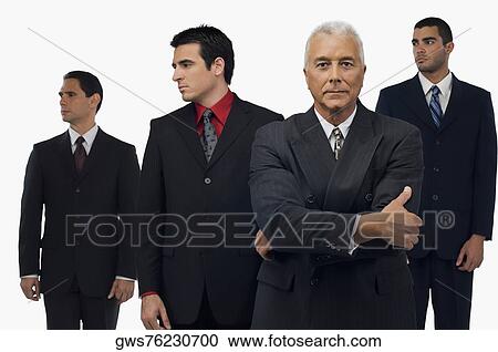 Businessman looking serious with three businessmen standing behind him and looking away View Large Photo Image Stock Image - Businessman looking serious with three businessmen standing behind him and looking away. Fotosearch