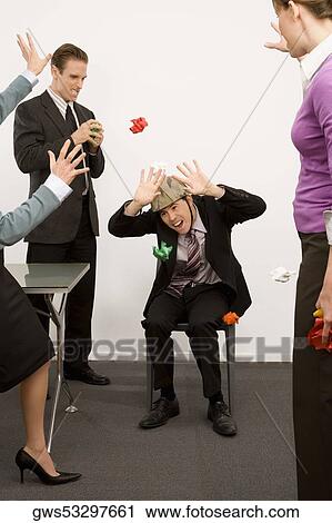 Stock Image - Businessman protecting himself from colleagues throwing paper balls. Fotosearch