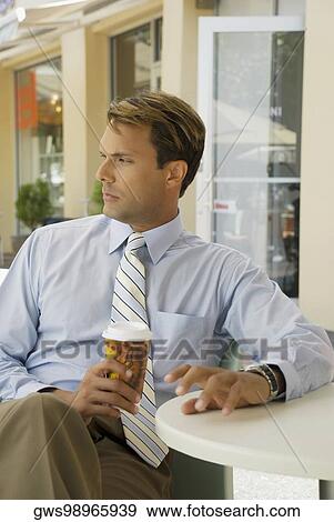 Stock Photo - Businessman sitting in a restaurant and holding a disposable cup. Fotosearch