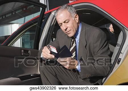 Stock Photograph - Businessman sitting in a taxi and checking his passport. Fotosearch