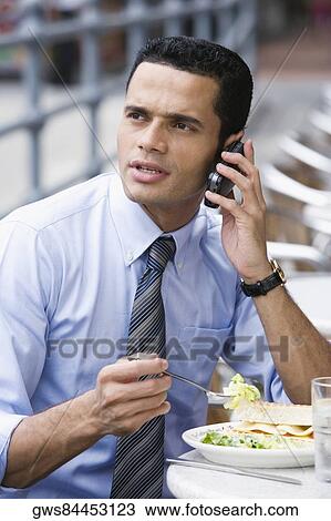 Businessman talking on a mobile phone during lunch View Large Photo Image Stock Image - Businessman talking on a mobile phone during lunch. Fotosearch