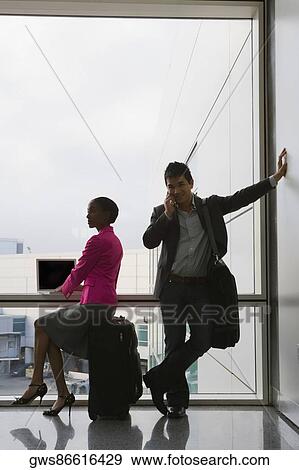 Businessman talking on a mobile phone with a businesswoman using a laptop beside him View Large Photo Image Stock Photo - Businessman talking on a mobile phone with a businesswoman using a laptop beside him. Fotosearch