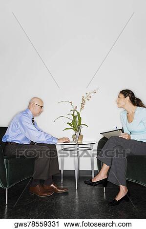 Stock Image - Businessman using a laptop with a businesswoman sitting in front of him. Fotosearch