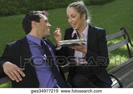 Businessman with a businesswoman having food on a park bench View Large Photo Image Stock Photo - Businessman with a businesswoman having food on a park bench. Fotosearch