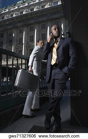 Stock Photograph - Businesswoman carrying a briefcase and a businessman talking on a mobile phone. Fotosearch