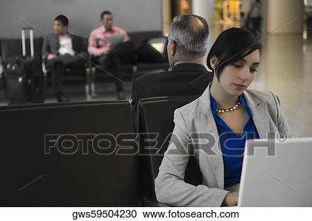 Businesswoman using a laptop with a businessman behind him at an airport View Large Photo Image Stock Image - Businesswoman using a laptop with a businessman behind him at an airport. Fotosearch