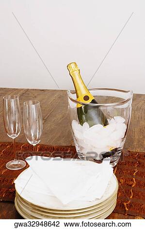 Champagne bottle in an ice bucket with champagne flutes and plates on a table View Large Photo Image Stock Image - Champagne bottle in an ice bucket with champagne flutes and plates on a table. Fotosearch