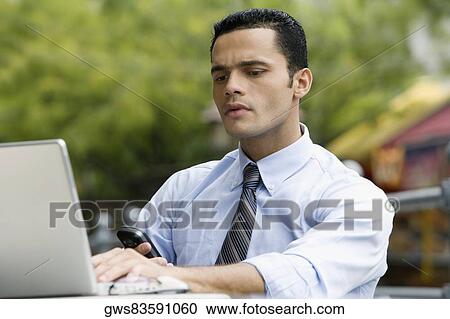 Close-up of a businessman checking his phone while using a laptop View Large Photo Image Stock Image - Close-up of a businessman checking his phone while using a laptop. Fotosearch