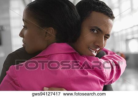 Close-up of a businessman embracing a businesswoman and winking at an airport View Large Photo Image Stock Photo - Close-up of a businessman embracing a businesswoman and winking at an airport. Fotosearch