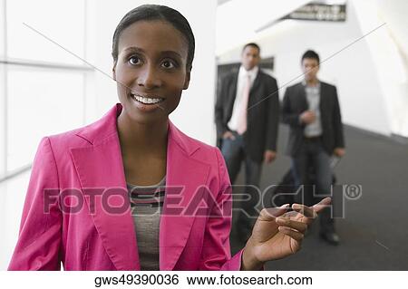 Close-up of a businesswoman smiling with two businessmen standing behind her at an airport View Large Photo Image Stock Photograph - Close-up of a businesswoman smiling with two businessmen standing behind her at an airport. Fotosearch
