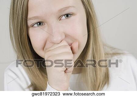 Stock Image - Close-up of a girl smiling with her hands covering her mouth. Fotosearch