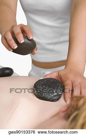 Stock Photograph - Close-up of a massage therapist placing pebbles on a woman's back. Fotosearch