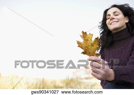 Stock Photo - Close-up of a mature woman holding a maple leaf and smiling. Fotosearch