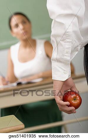 Stock Photography - Close-up of a person's hand holding an apple in front of a female teacher. Fotosearch