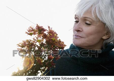 Stock Image - Close-up of a senior woman looking at bunch of flowers and smelling. Fotosearch