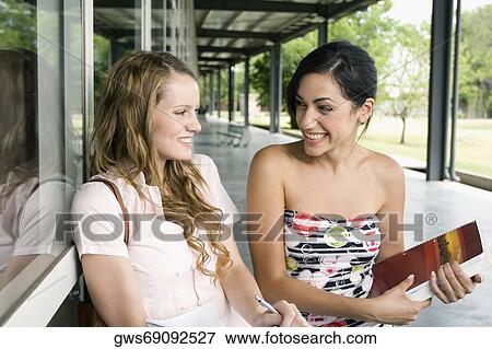 Stock Photo - Close-up of two young women sitting in a corridor and smiling. Fotosearch