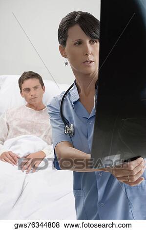 Female surgeon examining an X-Ray report with a patient in the background View Large Photo Image Stock Photo - Female surgeon examining an X-Ray report with a patient in the background. Fotosearch
