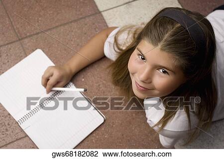 Stock Image - High angle view of a schoolgirl lying on the floor and smiling. Fotosearch