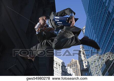 Stock Photo - Low angle view of a businessman jumping in mid-air and drinking. Fotosearch