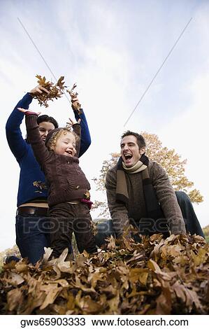 Stock Image - Low angle view of a couple and their daughter playing with leaves. Fotosearch
