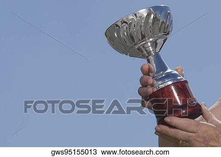 Stock Image - Low angle view of human hands holding a trophy. Fotosearch