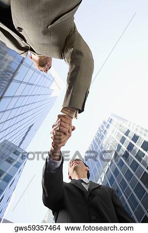 Low angle view of two businessmen shaking hands and smiling View Large Photo Image Picture - Low angle view of two businessmen shaking hands and smiling. Fotosearch