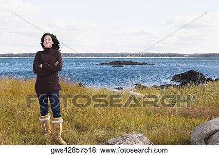 Stock Photo - Mature woman standing on the beach with her arms crossed. Fotosearch