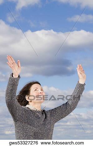 Mature woman standing with her arms raised and looking up View Large Photo Image Stock Photograph - Mature woman standing with her arms raised and looking up. Fotosearch