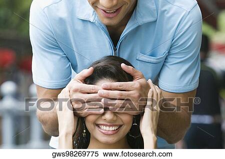 Stock Photography - Mid adult man covering eyes of a young woman with his hands. Fotosearch