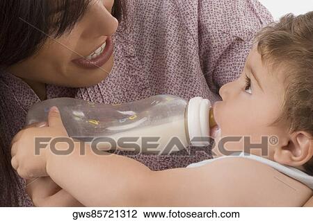 Stock Image - Mid adult woman feeding her son with a baby bottle and smiling. Fotosearch