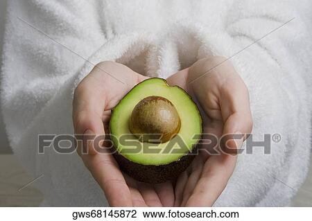 Stock Image - Mid section view of a person's hands holding a half of avocado. Fotosearch