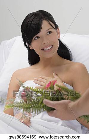 Stock Photo - Person's hand giving a bouquet of flowers to a young woman sitting on the hospital bed. Fotosearch