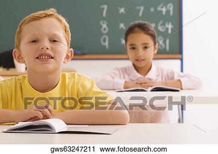 Stock Image - Portrait of a boy and a girl sitting in a classroom. Fotosearch