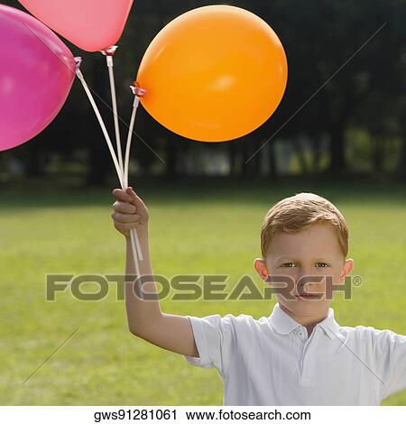 Stock Image - Portrait of a boy holding balloons in a park. Fotosearch