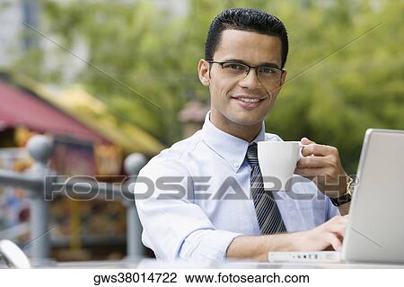 Stock Image - Portrait of a businessman drinking coffee while using a laptop. Fotosearch